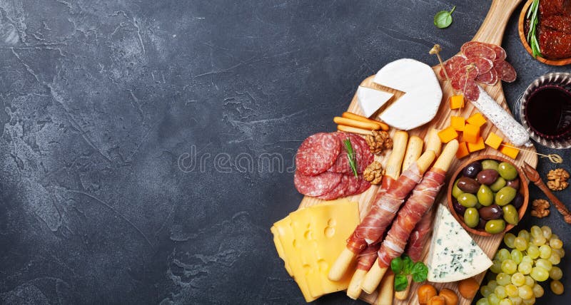 Italian appetizers or antipasto set with gourmet food on black stone table top view. Mixed delicatessen of cheese and meat snacks. Format of the banner. Italian appetizers or antipasto set with gourmet food on black stone table top view. Mixed delicatessen of cheese and meat snacks. Format of the banner