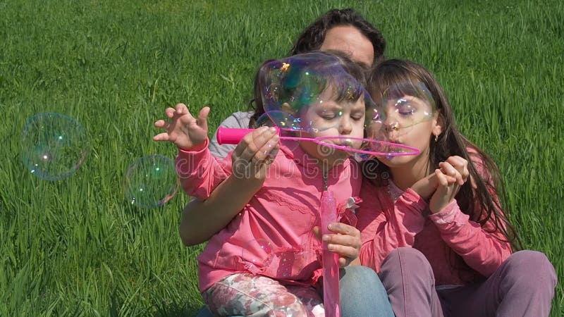 Crianças com a mãe estão brincando com bolhas de sabão Feliz família sobre a natureza no verão Garota com crianças no parque em u