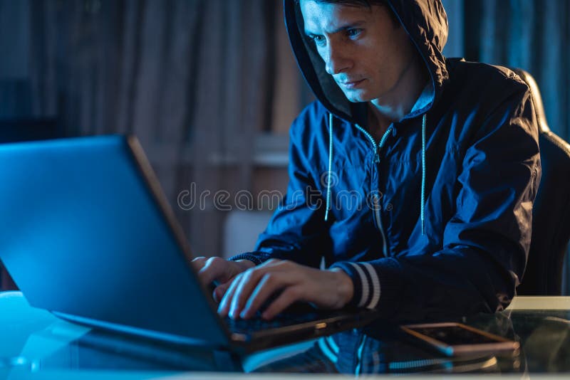 Cybercriminal hacker in the hood typing program code while stealing access databases with passwords. The concept of cyber security. Cybercriminal hacker in the hood typing program code while stealing access databases with passwords. The concept of cyber security