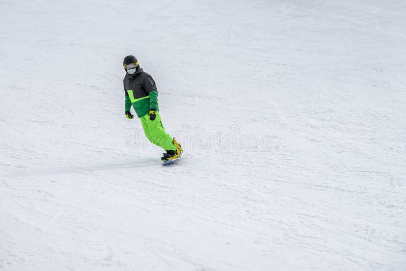 Unrecognizable snowboarder skiing in bright green suit, protective glasses mask on the slope, overalls. Winter sport concept and leisure outdoor lifestile. Minimalism. Winter background, copy space. Unrecognizable snowboarder skiing in bright green suit, protective glasses mask on the slope, overalls. Winter sport concept and leisure outdoor lifestile. Minimalism. Winter background, copy space