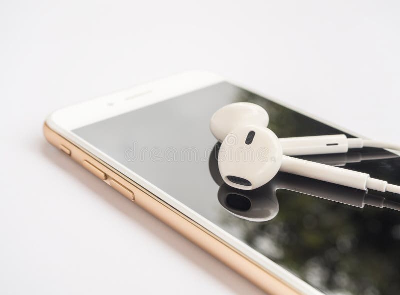 Close-up image of earbuds on top of gold smartphone and reflection on screen isolate on white background. Close-up image of earbuds on top of gold smartphone and reflection on screen isolate on white background