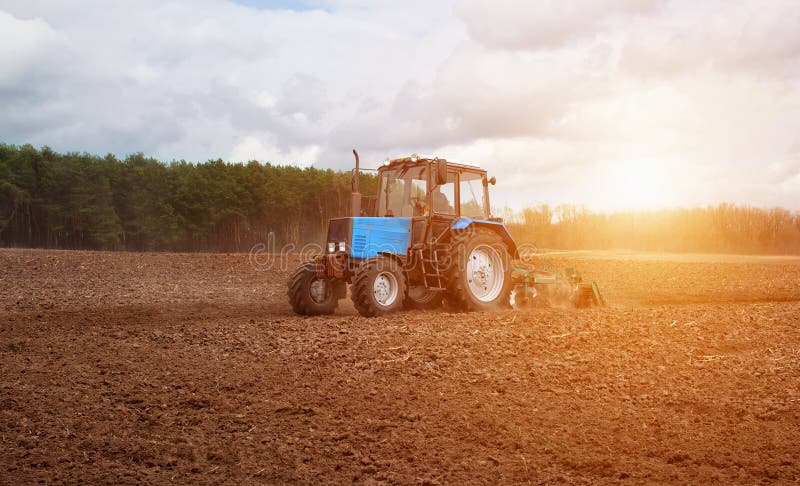 In the early,spring morning,because of the wood the bright sun ascends.The tractor goes and pulls a plow,plowing a field before la royalty free stock image In the early,spring morning,because of the wood the bright sun ascends.The tractor goes and pulls a plow,plowing a field before la royalty free stock image
