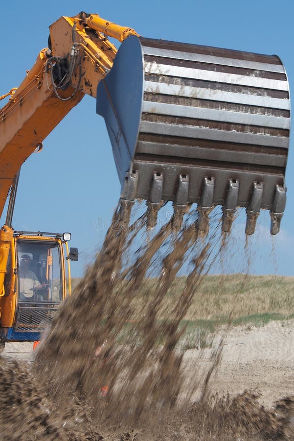 Action shot of an orange digger/earth mover with falling sand from its claw