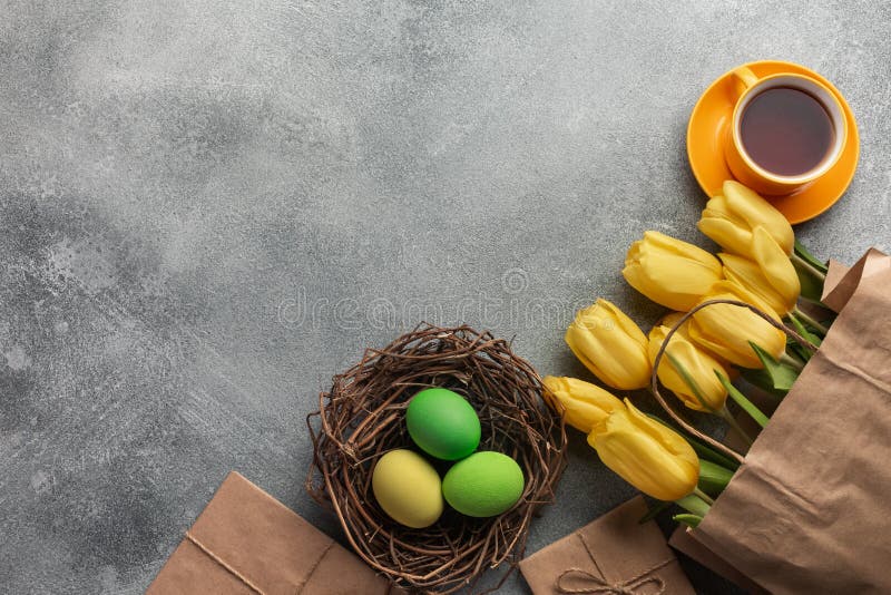 Easter background with blue, green eggs and a cup of tea in nest and yellow tulips. Top view with copy space