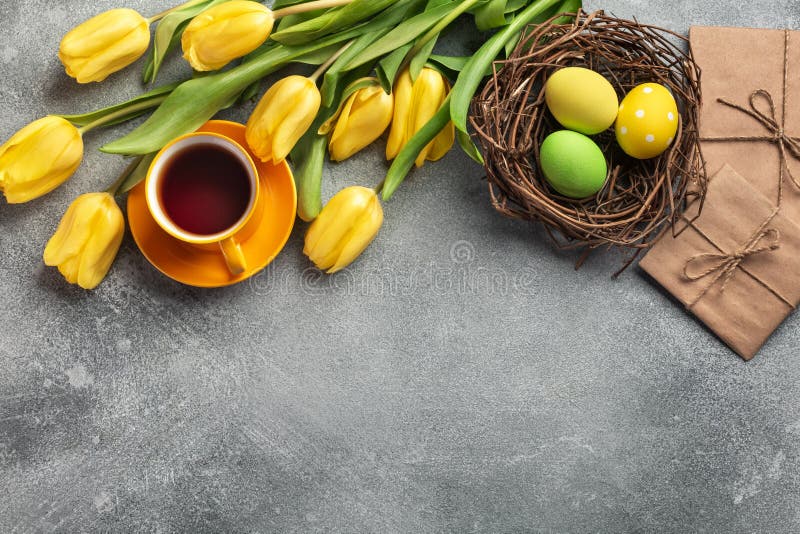 Easter background with blue, green eggs and a cup of tea in nest and yellow tulips. Top view