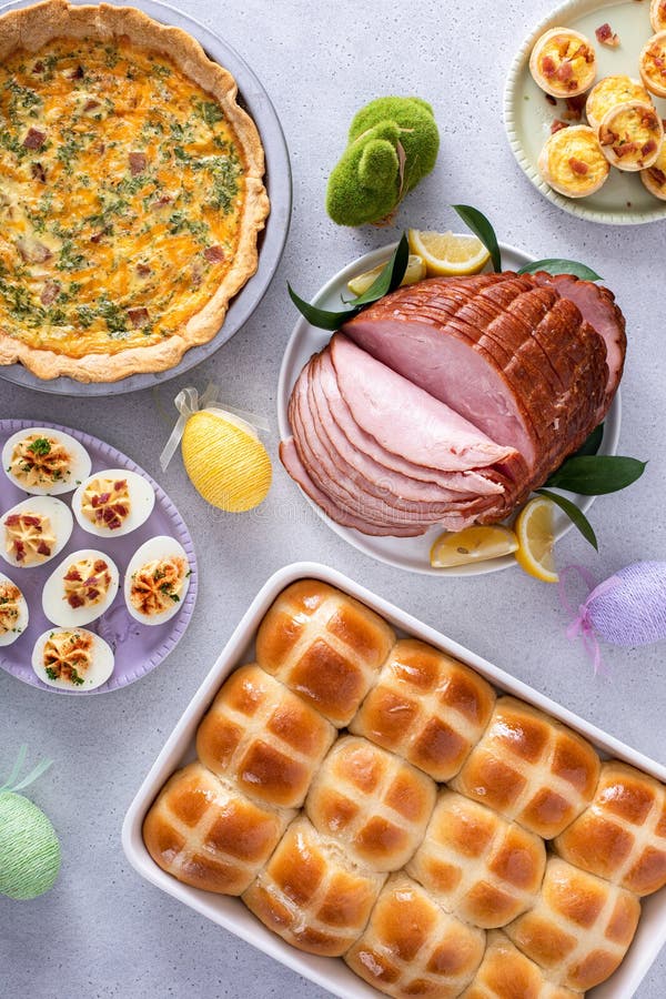 Easter brunch on large table with spiral sliced ham, quiche, deviled eggs and hot cross buns stock photography