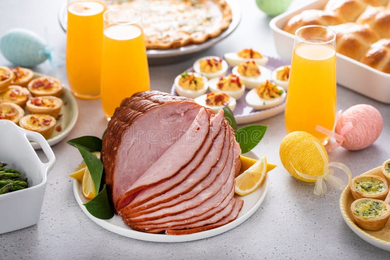 Easter brunch on large table with spiral sliced ham, quiche, deviled eggs and hot cross buns royalty free stock images