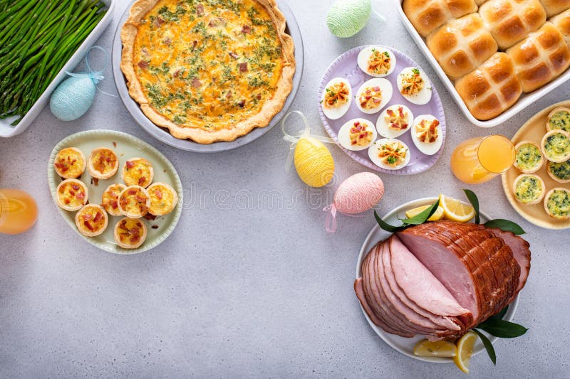 Easter brunch on large table with spiral sliced ham, quiche, deviled eggs and hot cross buns royalty free stock image