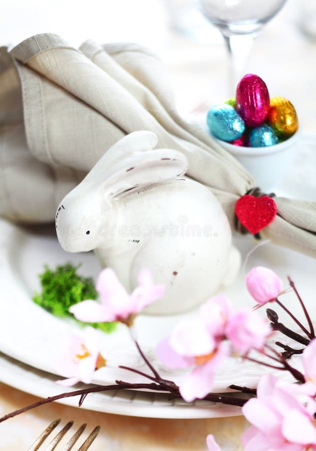 View across cherry blossom to a table setting with a white Easter Bunny and tiny colourful chocolate easter eggs. View across cherry blossom to a table setting with a white Easter Bunny and tiny colourful chocolate easter eggs