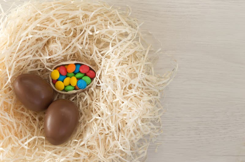 Easter. Chocolate eggs with multicolored candies lie in a nest on a wooden white table royalty free stock photos Easter. Chocolate eggs with multicolored candies lie in a nest on a wooden white table royalty free stock photos