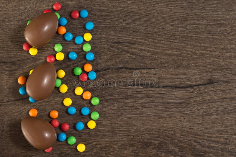Easter. Chocolate eggs with multicolored candies lie on a wooden brown table royalty free stock image Easter. Chocolate eggs with multicolored candies lie on a wooden brown table royalty free stock image