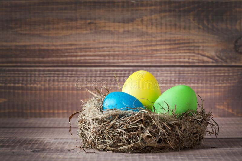 Easter color eggs in nest on wood