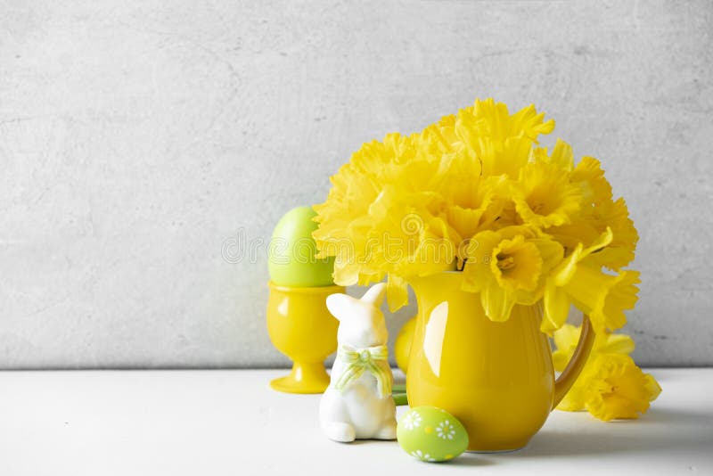 Easter composition with Easter eggs, bunny and Bouquet of yellow daffodils in a yellow jug on table top, home decor