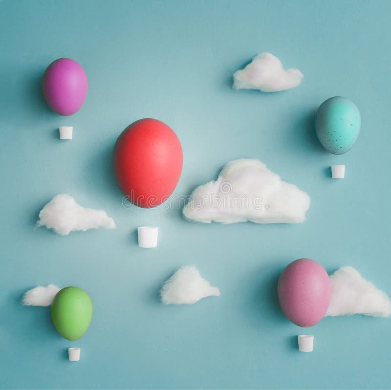 Easter composition made of Hot air balloons made and decorated Easter eggs with cotton clouds on bright blue background. Flat lay