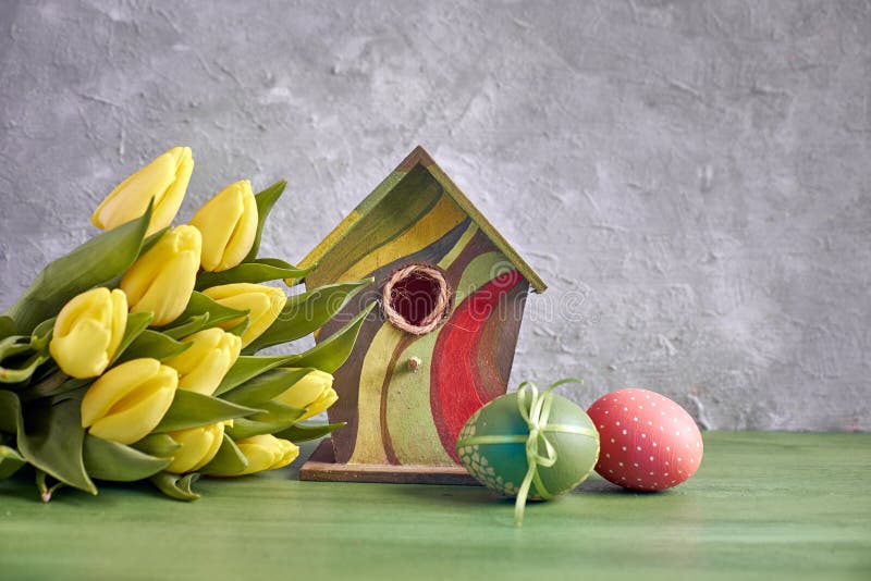 Easter decorations on gray concrete background. Yellow tulips, birdhouse and painted Easter eggs royalty free stock photo