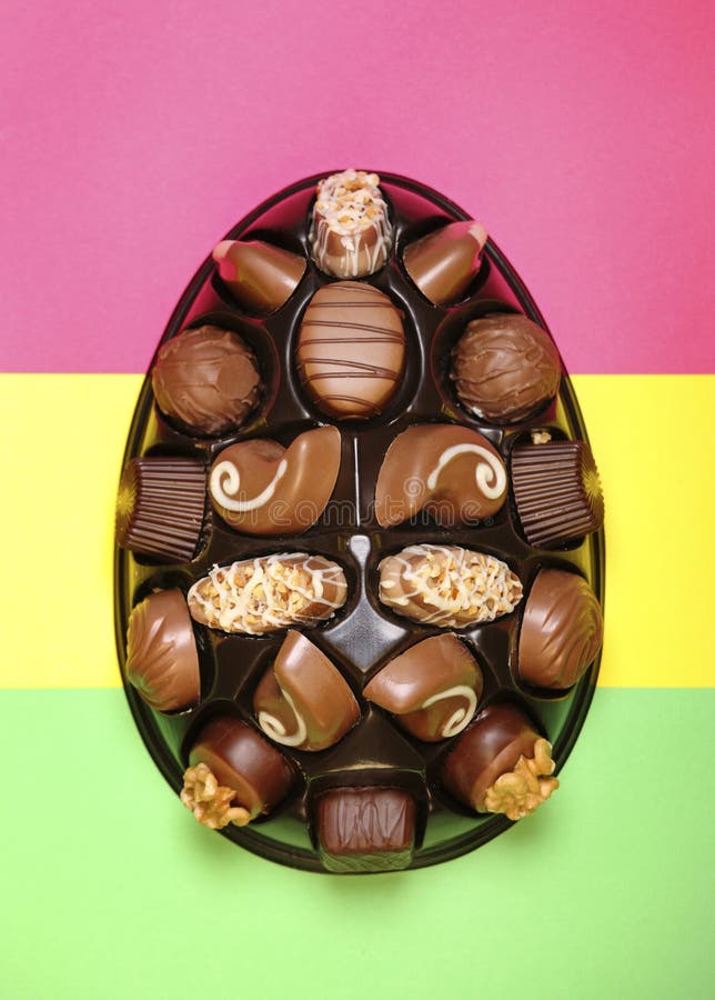 A close-up of high quality swiss chocolates in the shape of an egg over pink, yellow and green background. A close-up of high quality swiss chocolates in the shape of an egg over pink, yellow and green background