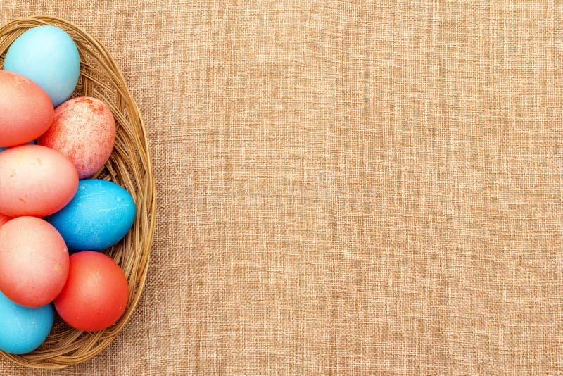 Easter eggs concept, table arrangement decoration. Pink rosy and blue eggs in wicker basket on cloth linen background, top view