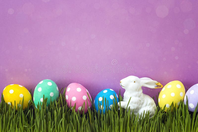 Easter eggs with a decorative hare in fresh green grass on purple background.