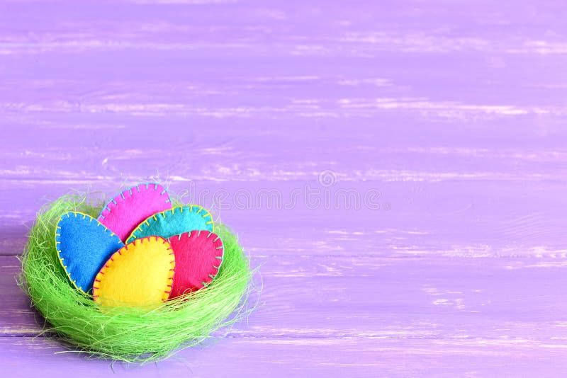 Easter eggs in a nest. Felt Easter eggs set in a green sisal nest isolated on purple wooden background with copyspace for text