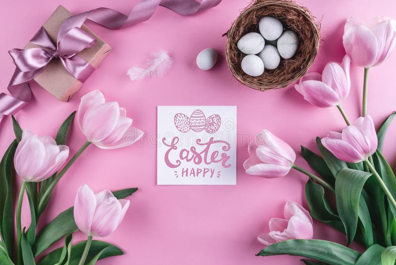 Easter eggs in nest and tulips flowers on pink background with Easter card.