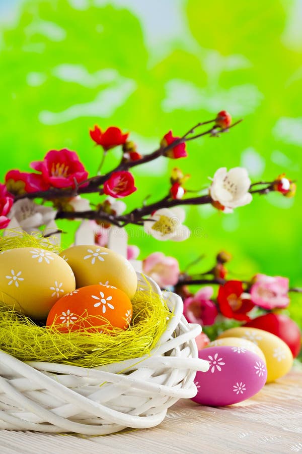 Easter eggs in the nest on wooden table and flowers on green background
