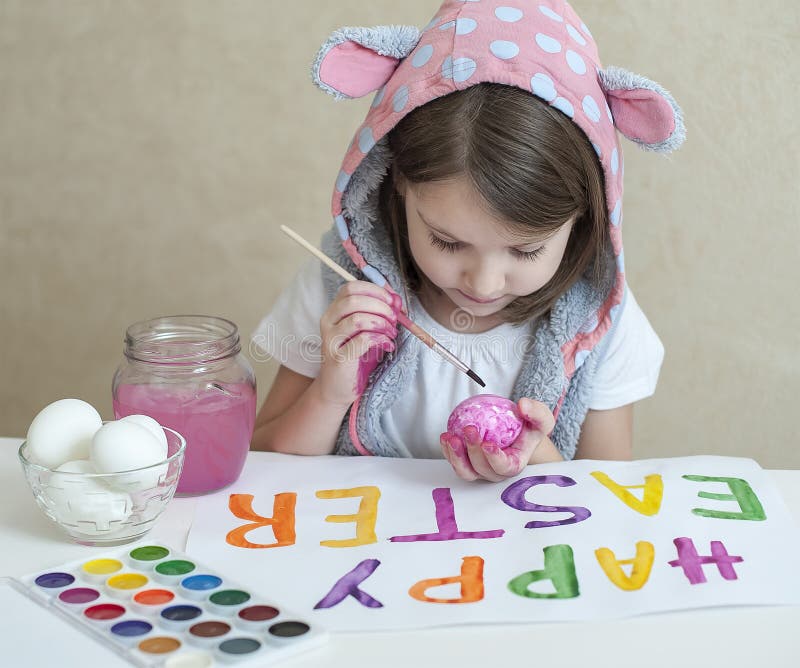 Easter feliz Pintor da menina nas orelhas cor-de-rosa do coelho com os ovos pintados coloridos Uma criança que prepara-se para a imagem de stock Easter feliz Pintor da menina nas orelhas cor-de-rosa do coelho com os ovos pintados coloridos Uma criança que prepara-se para a imagem de stock