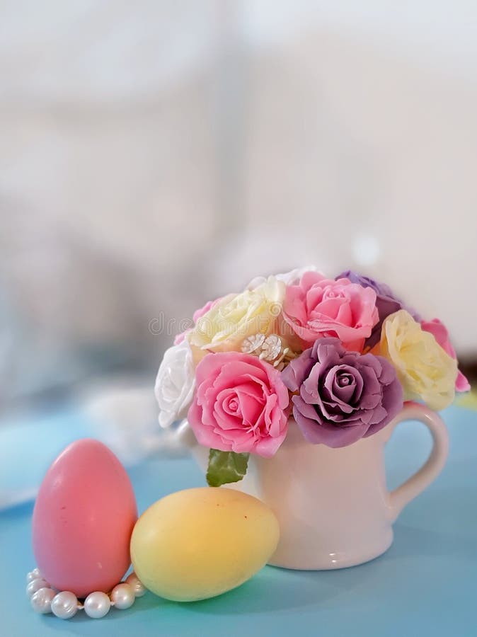 Easter holiday greeting concept. Bouquet of roses in decorative vase, colorful eggs on blue surface on blurred background. Handmade soap romantic composition stock images Easter holiday greeting concept. Bouquet of roses in decorative vase, colorful eggs on blue surface on blurred background. Handmade soap romantic composition stock images