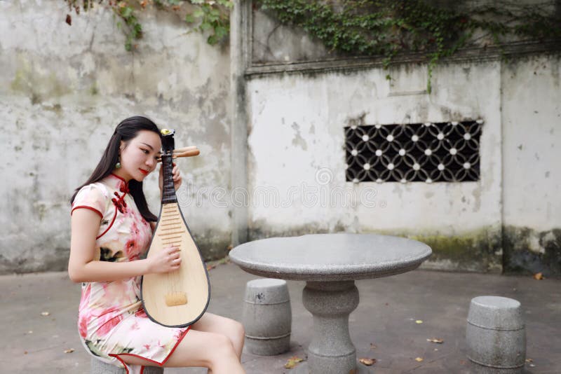 Eastern Chinese woman artist traditional chi-pao cheongsam in a garden play musical instruments pipa lute ancient historic stock photography Eastern Chinese woman artist traditional chi-pao cheongsam in a garden play musical instruments pipa lute ancient historic stock photography