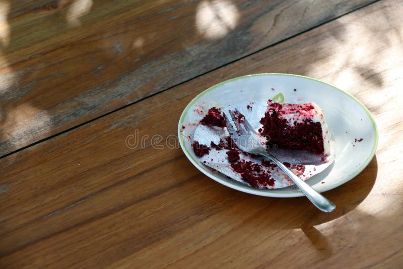 Eaten cake in the white plate with small spoon on the wooden table.