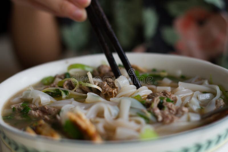 eating a bowl of Vietnamese beef noodle soup Pho Bo with chop sticks