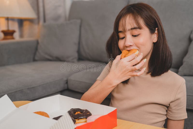 Eating donut when takeout and delivery. Fast food takeaway back home. Asian woman lifestyle in living room. Social distancing