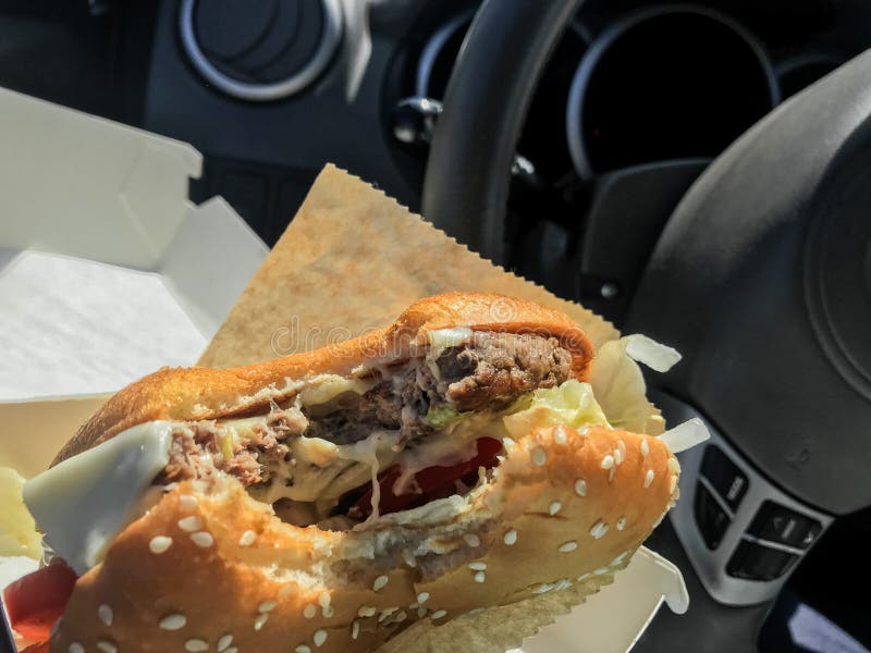 Eating while Driving a Bitten Burger in the Hands Inside the Car