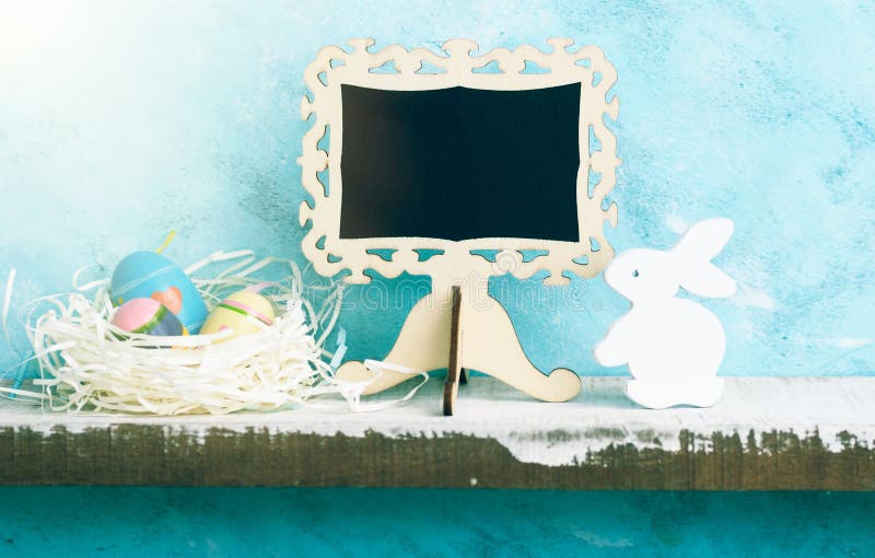 Eatser mock up with chalkboard, painted eggs in nest and white wooden bunny on shelf against blue wall. Scandinavian style royalty free stock photo