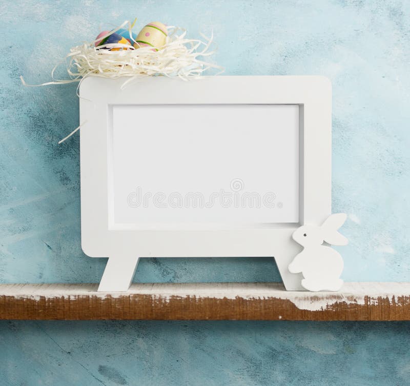 Eatser mock up with photoframe, painted eggs in nest and white wooden bunny on shelf against blue wall. Scandinavian style royalty free stock images