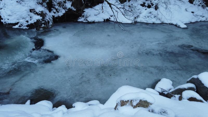 Eau coulant sous la glace dans la forêt de montagne pendant un froid extrême en hiver banque de vidéos