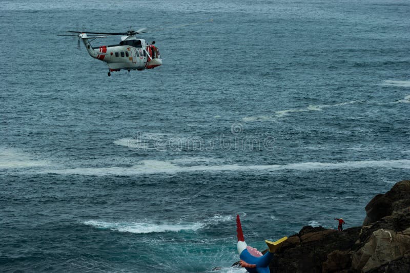 An ec225 Super Puma helicopter supervises a rescuer`s descent to the rocks