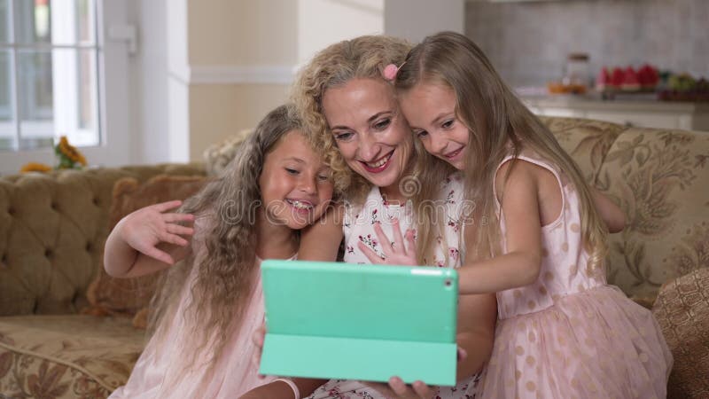 Eccitata donna caucasica e ragazze che salutano al rallentatore, sorridendo i messaggi online su una video chat su una tavoletta. archivi video