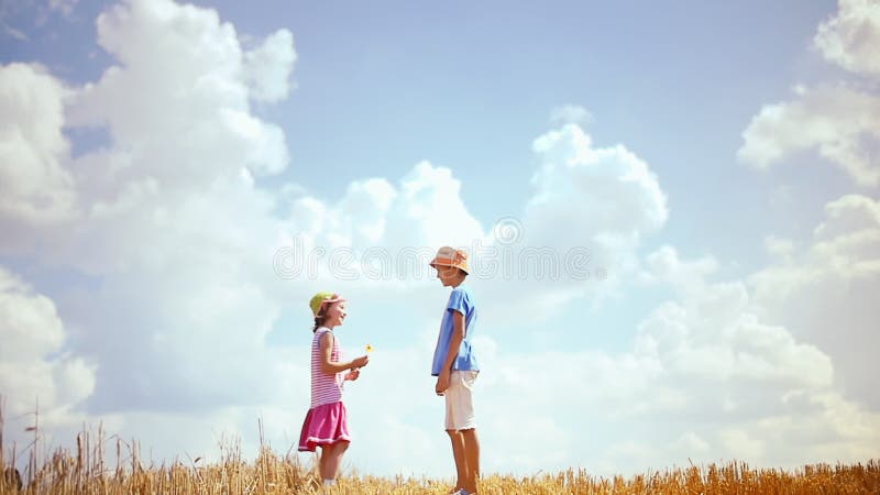 Echt moment : jongen die een bloem aanbiedt aan een meisje op een heuvel tegen een picturesque hemel