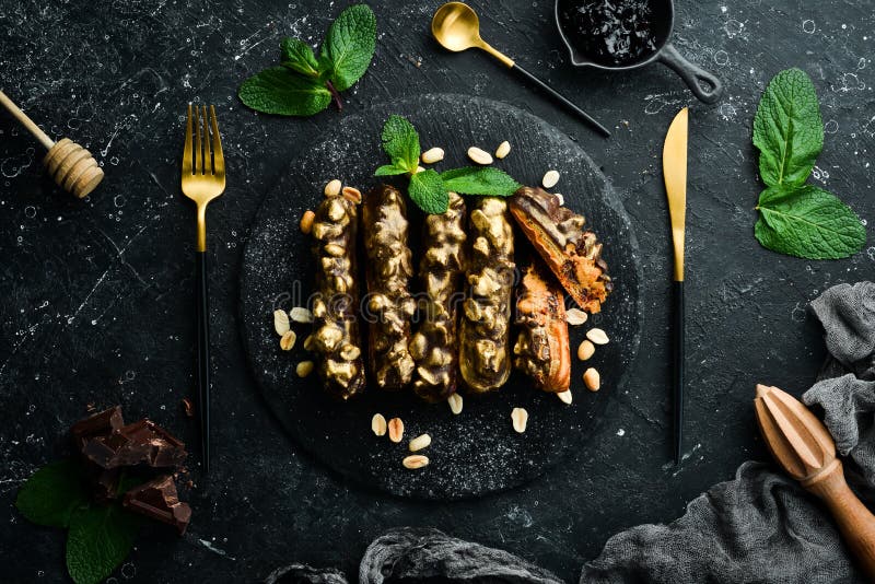 Eclair with chocolate-peanut cream. Chocolate and nut dessert on a black stone plate. Top view. Rustic style