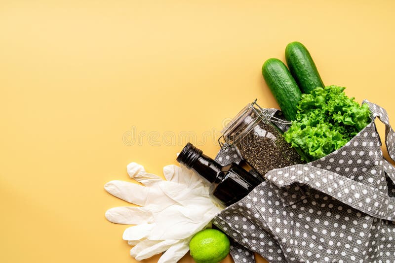 Eco friendly bag with green vegetables, chia seeds, gloves and olive oil top view on orange background with copy space.