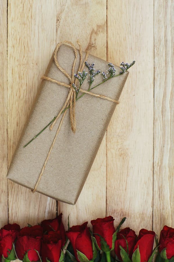 Eco friendly brown paper wrapped gift box present decorated with rose and other flowers on wooden background, valentine ornamental royalty free stock photography Eco friendly brown paper wrapped gift box present decorated with rose and other flowers on wooden background, valentine ornamental royalty free stock photography