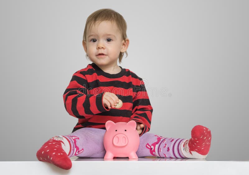 Economias e conceito da operação bancária A menina da criança está pondo moedas no banco leitão do dinheiro fotografia de stock royalty free Economias e conceito da operação bancária A menina da criança está pondo moedas no banco leitão do dinheiro fotografia de stock royalty free
