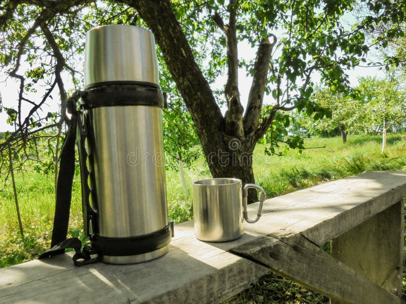 Edelstahlthermosflasche- und -schalenstand auf einer Bank im Garten im Sommer stockbild Edelstahlthermosflasche- und -schalenstand auf einer Bank im Garten im Sommer stockbild