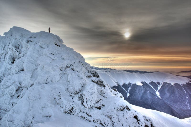 Uno scalatore sulla cima della montagna, guardando uno splendido tramonto in inverno.