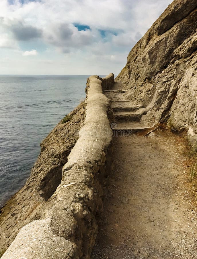 Edge of the cliff with an ancient stone path along the sea with stone steps against the sea and clouds, vertical frame stock photo Edge of the cliff with an ancient stone path along the sea with stone steps against the sea and clouds, vertical frame stock photo