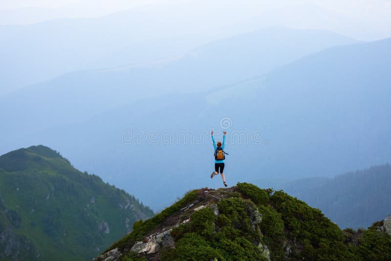 At the edge of the cliff there is a small lawn with the rocks. The tourist girl jumps full of happiness. The high mountains. royalty free stock images At the edge of the cliff there is a small lawn with the rocks. The tourist girl jumps full of happiness. The high mountains. royalty free stock images