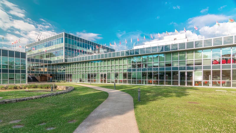 Modern low rise glass office building in business district and green lawn with path in inner yard timelapse hyperlapse. Flags of many different countries on the top of roof. Modern low rise glass office building in business district and green lawn with path in inner yard timelapse hyperlapse. Flags of many different countries on the top of roof