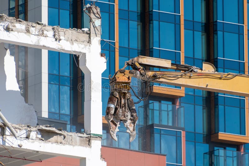 Edifício de demolição por escavação com ferramenta hidráulica perto de uma estrutura de vidro moderna foto de stock
