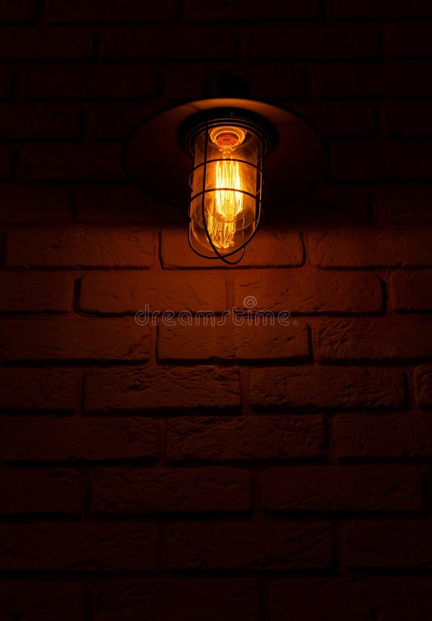 Edison bulb in a street lamp. Antique lantern on a brick wall. Warm cozy light in the dark. Light and shadows stock photography