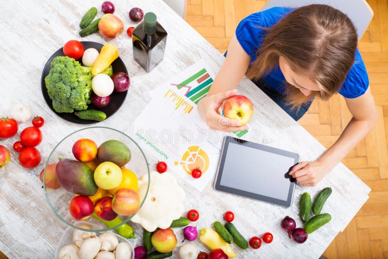 A young adult woman informing herself with a tablet PC about nutritional values of fruits and vegetables. A young adult woman informing herself with a tablet PC about nutritional values of fruits and vegetables.